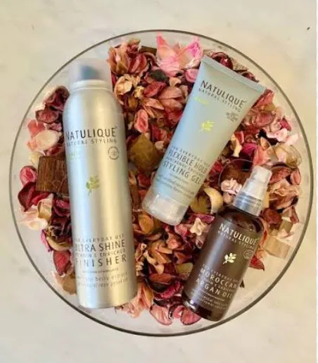 Natulique Naturkosmetik-Produkte: Ultra Shine Finisher, Flexible Hold Styling Gel und Moroccan Argan Oil, dekorativ auf Blütenblättern präsentiert