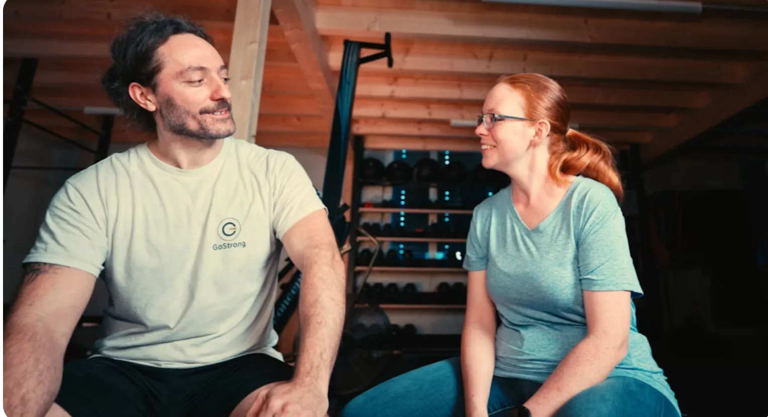GoStrong Coach bespricht lächelnd mit einem Kunden eine Übung am Boden